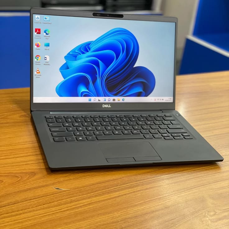 Dell Latitude open on wooden desk showing Windows 11 blue flower wallpaper - front angle view