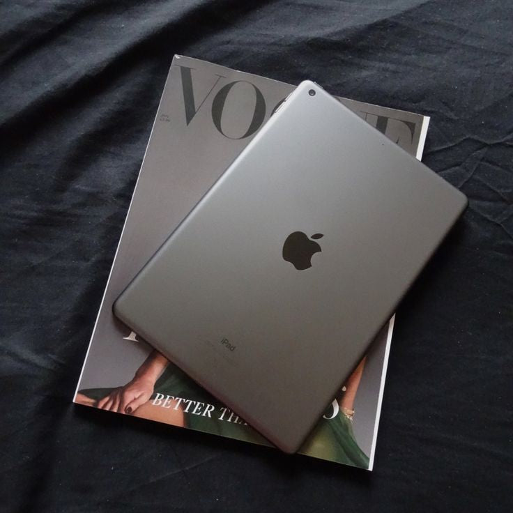 Apple iPad 8th Generation Space Gray back view resting on Vogue magazine on dark fabric