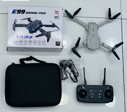 E99 Drone Pro gray unboxed showing drone, remote controller, carrying case, spare propellers and original box on white floor