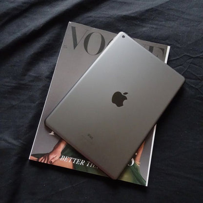 Apple iPad 8th Generation Space Gray back view resting on Vogue magazine on dark fabric
